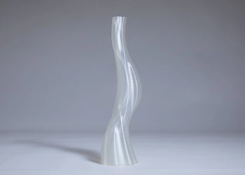 The Argot Studio Les Hortenses Vase, Tall stands upright on a plain light surface with a gray background, showcasing its translucent and wavy 3D-printed form.