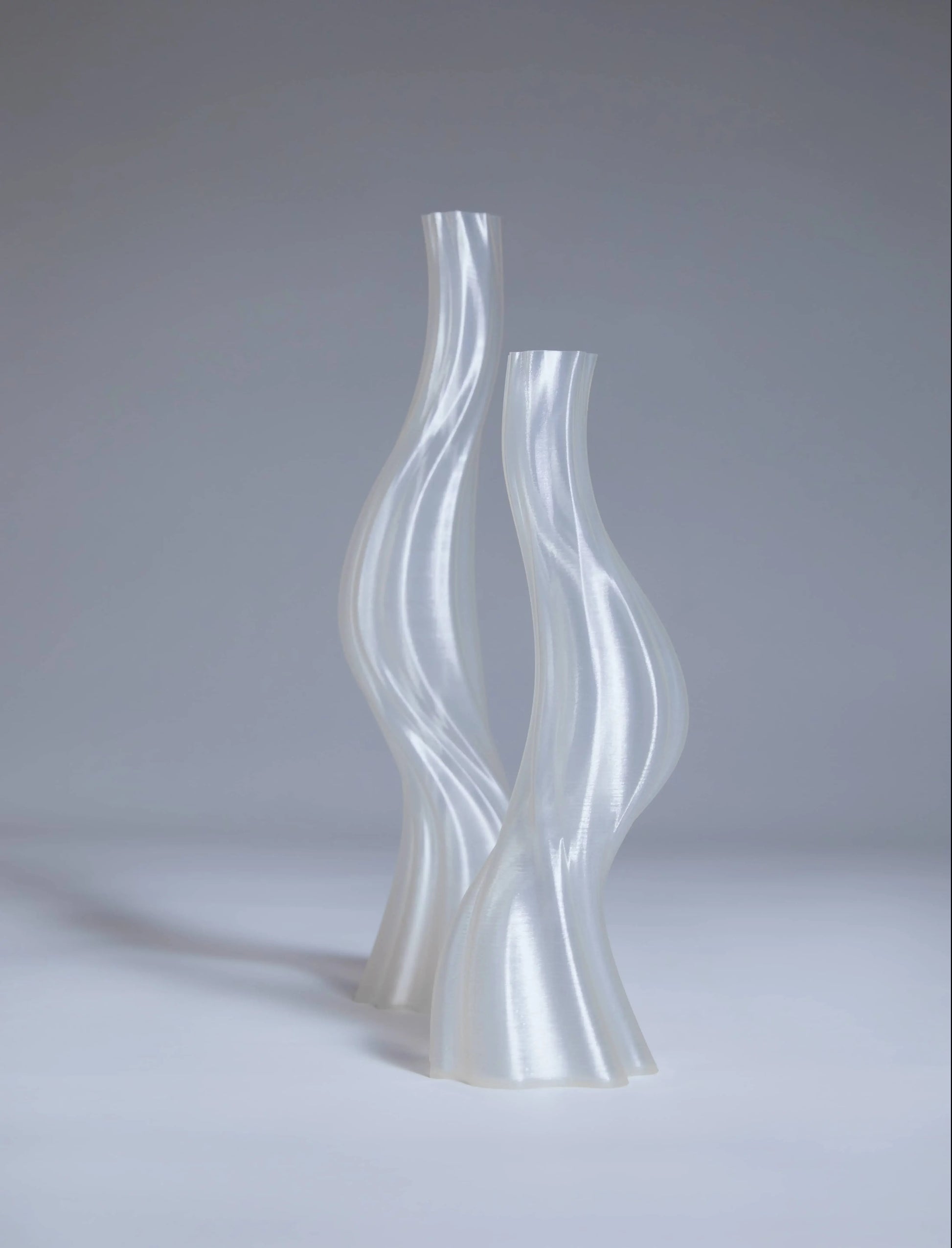 Two tall, translucent Argot Studio Les Hortenses Vases stand side by side against a light gray background, highlighting the contemporary 3D printed design and glossy finish by Argot Studio.