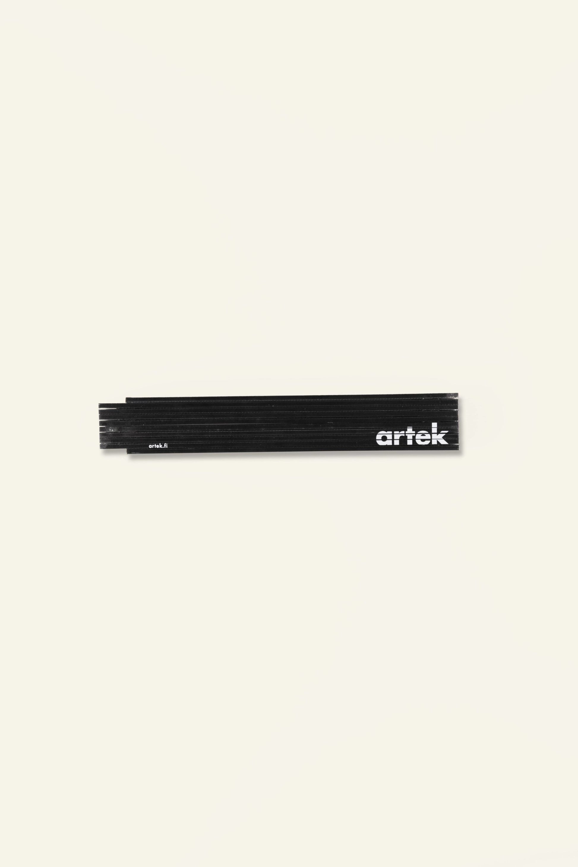 The Artek Folding Ruler, a black wooden tool featuring white Artek branding, rests closed on a plain light surface—perfect for taking precise measurements.