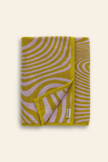 A BAGGU Bath Towel by BAGGU, folded to reveal its yellow and lavender wavy line pattern and a white edge tag with the brand name, is displayed on a light beige background.
