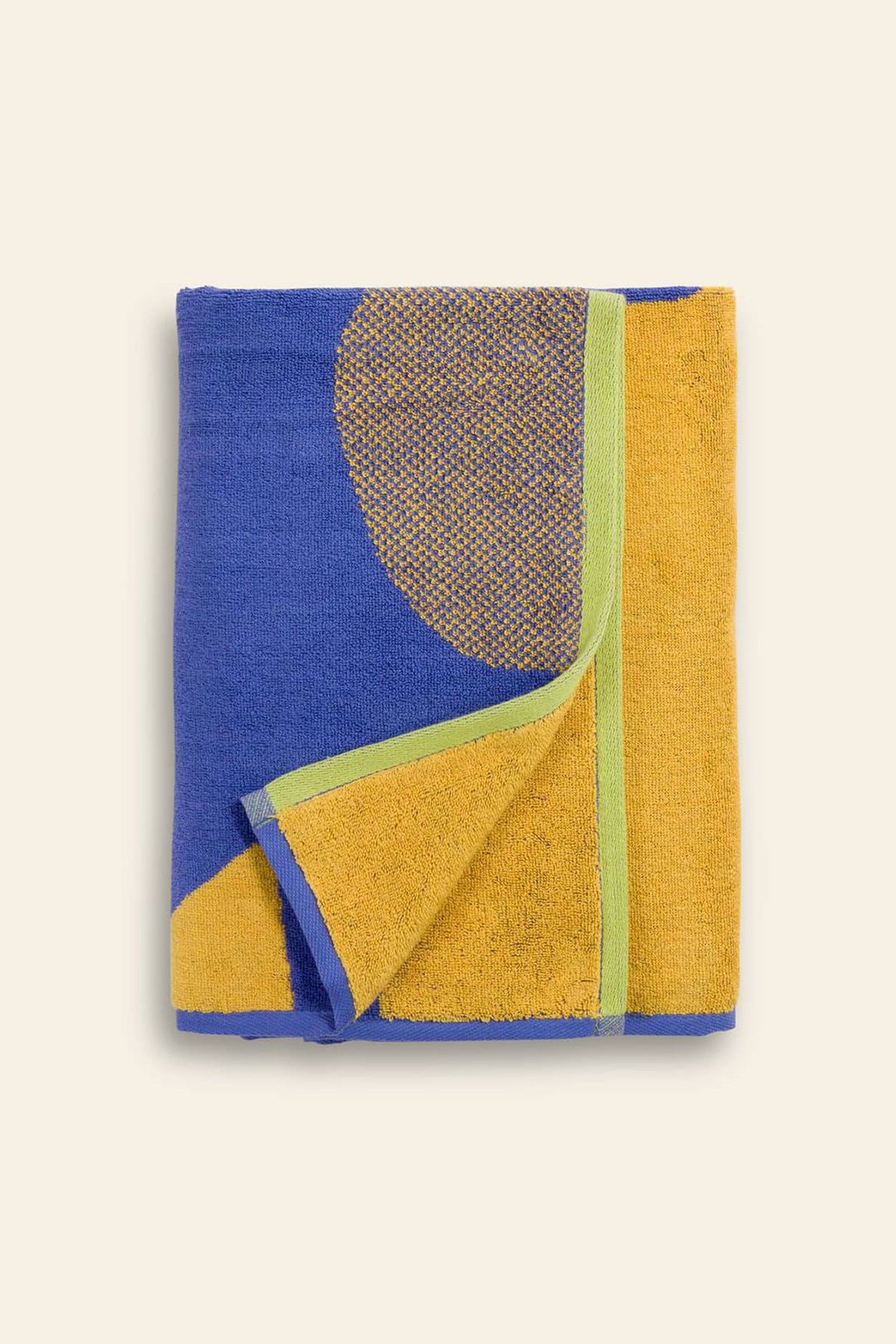The BAGGU Bath Towel features a bold geometric sunflower design in blue, yellow, and green with a large yellow semicircle on a blue background.