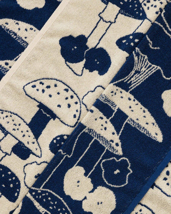 A close-up of fabric with blue and white mushrooms, round shapes, and subtle smiley faces in a whimsical pattern—perfect for a cheerful cleanup with the BAGGU Hand Towel Set of 2 by BAGGU.