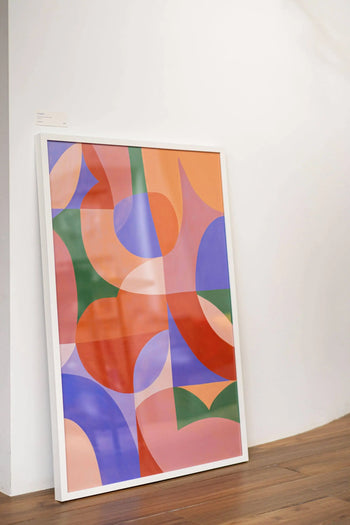 The Bbblob Amplify, 2020 Fine Art Print (50x70) by Bbblob showcases an abstract landscape of overlapping orange, purple, pink, red, green, and blue shapes leaning against a white wall on a wooden floor.