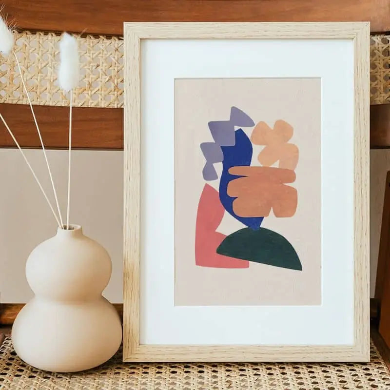 The Bbblob Floating In Mid Air, 2020 - Giclee Print (21x30) by Bbblob stands framed on a woven surface beside a matte beige vase with three dried white grasses, set against warm wooden tones for a peaceful ambiance.