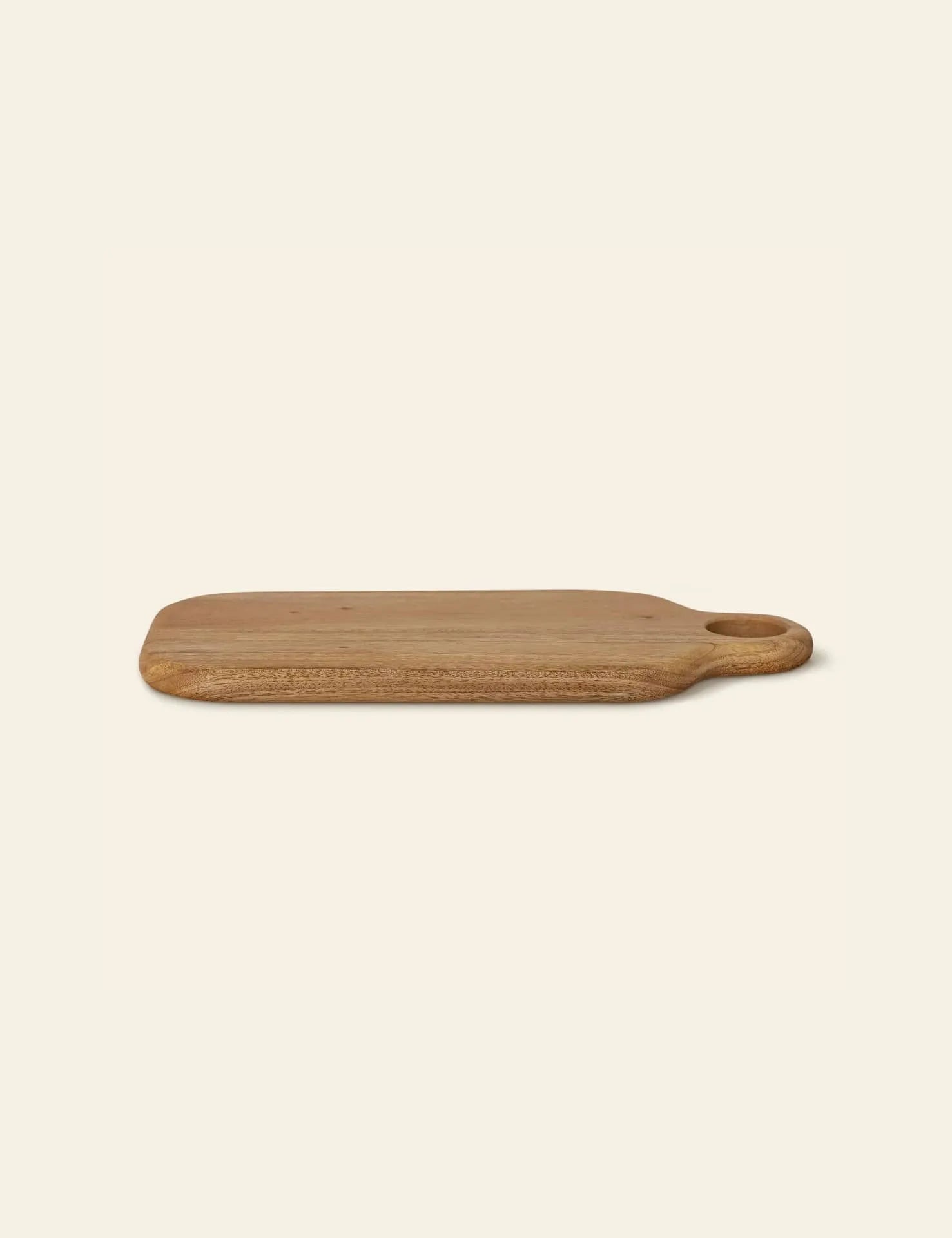 The Bloomingville Abbas Cutting Board by Bloomingville is a rectangular mahogany board with rounded edges and an oval handle, ideal for meal preparation, shown on a plain light background.