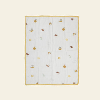 The Bloomingville Agnes Blanket by Bloomingville is a white muslin baby blanket with a yellow scalloped border and small prints of rainbows, suns, mushrooms, clouds, and animals on a light background.