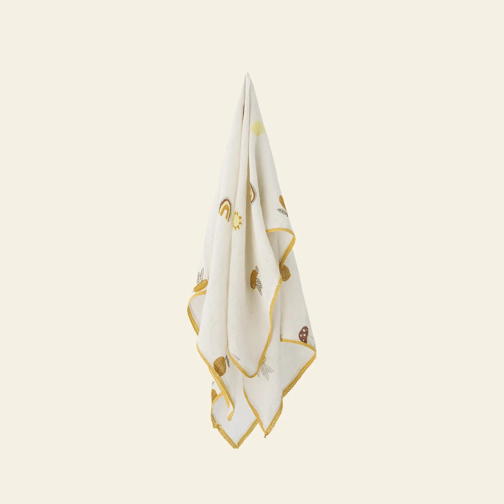 The Bloomingville Agnes Blanket by Bloomingville is a white baby blanket with yellow trim, featuring cute rainbows, suns, snails, and mushrooms, displayed against a simple beige background.