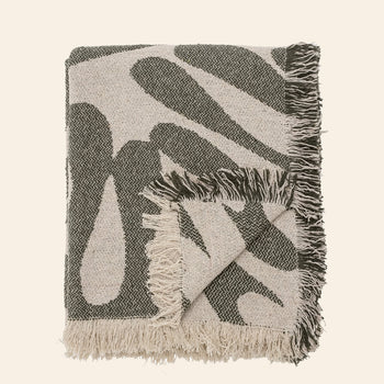 The Bloomingville Alk Throw by Bloomingville is a folded woven blanket made from recycled cotton, featuring a minimalist black and beige pattern with fringed edges, shown against a plain light background.