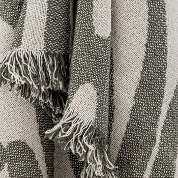 A close-up of the Bloomingville Alk Throw by Bloomingville, showcasing its minimalist woven pattern with fringed edges, featuring dark green and light gray stripes and curves in a versatile color palette.