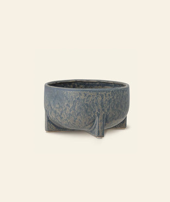 The Bloomingville Beryl Flowerpot by Bloomingville is a round, blue-gray pot with a textured finish and four short legs, ideal for greenery or decor. Photographed against an off-white background.