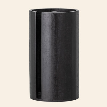 The Bloomingville Celian Kitchen Paper Stand by Bloomingville is a tall, cylindrical piece in dark paulownia wood with an open vertical slot and visible wood grain, exuding Scandinavian style against a plain light background.