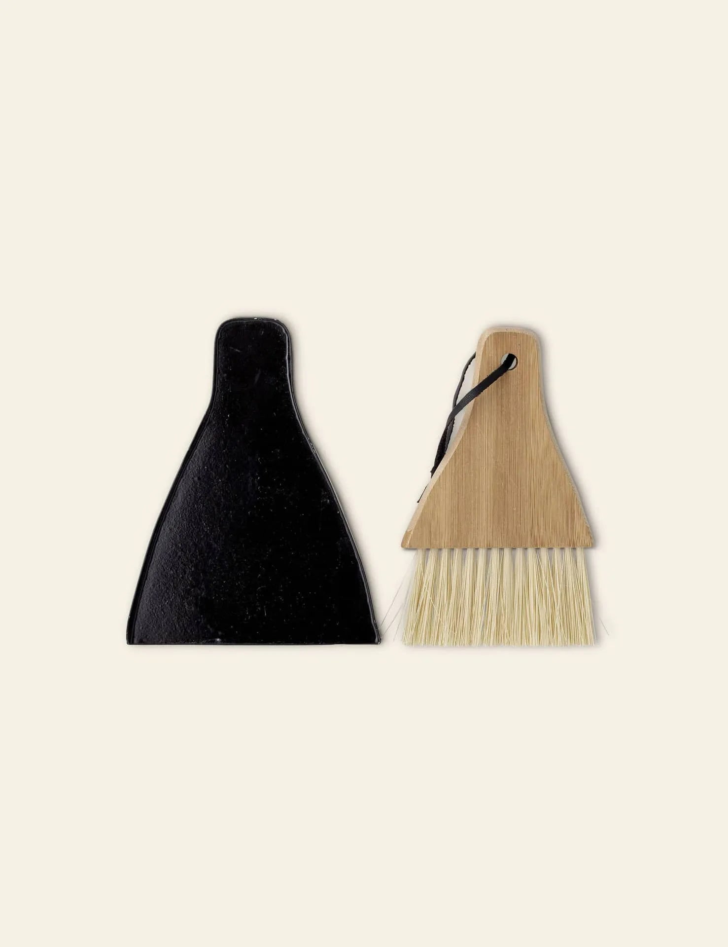 The Bloomingville Cleaning Dustpan & Broom, featuring a wooden handle and light bristles, sits beside its minimalist black dustpan on a beige background. This set by Bloomingville is perfect for efficient household cleaning.