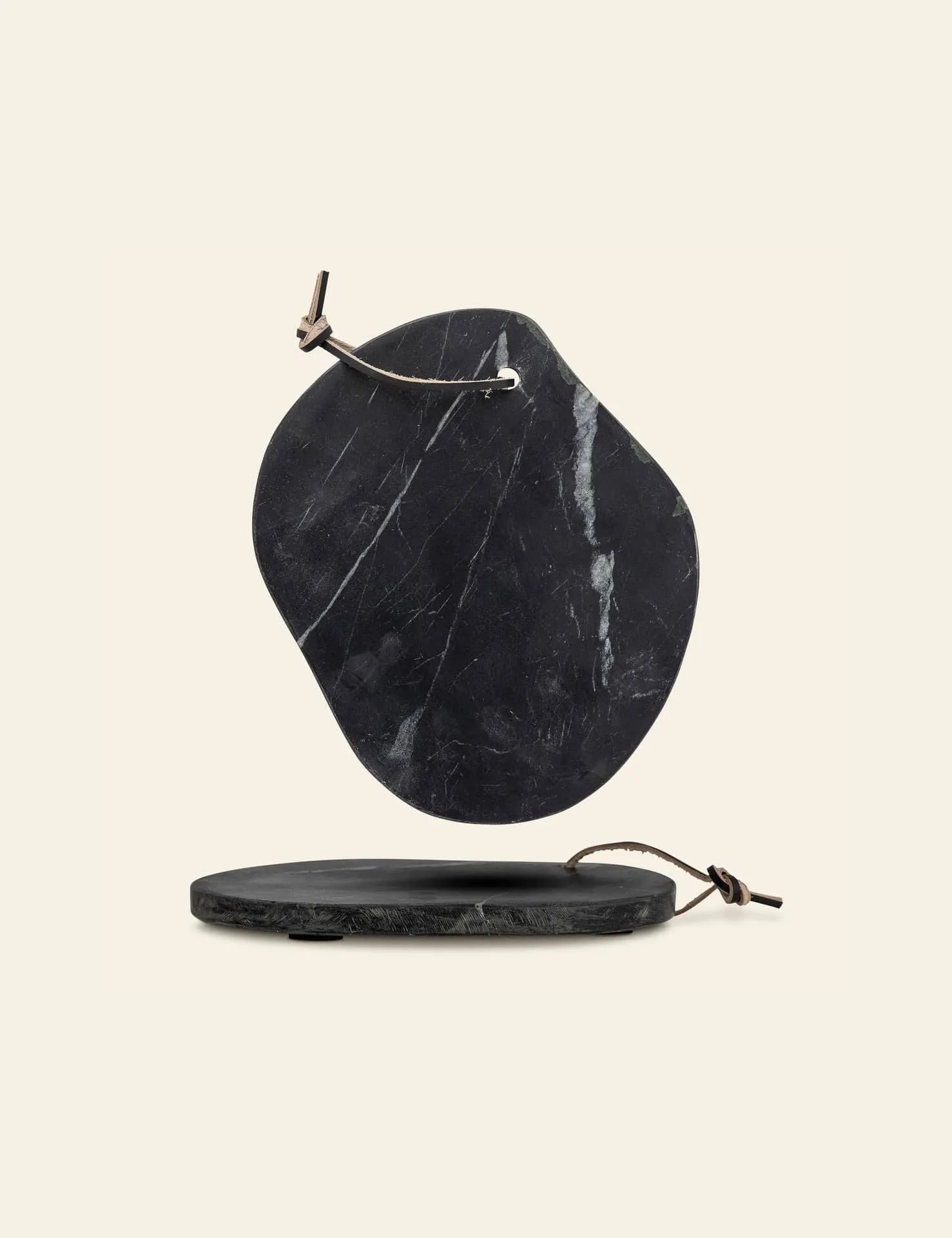 The Bloomingville Daris Cutting Board set by Bloomingville includes two irregular marble boards with smooth surfaces, natural veining, and leather hanging ties, shown on a light beige background.