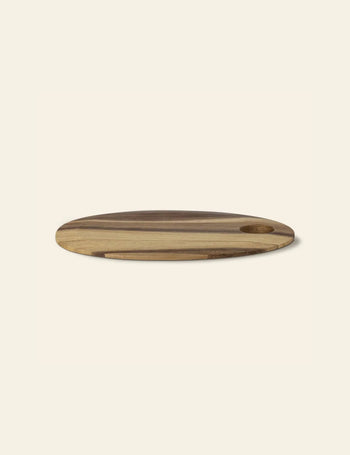 The Bloomingville Guti Cutting Board by Bloomingville is a round suar wood kitchen accessory with a handy hole near the edge, shown on a light beige background.