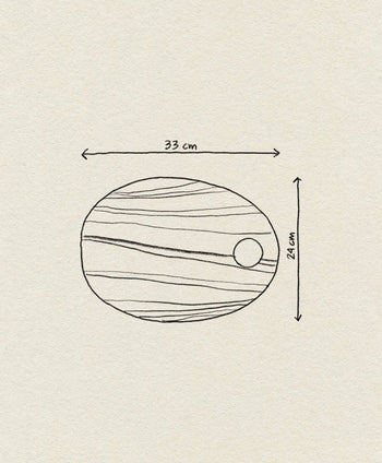 A simple line drawing of the Bloomingville Guti Cutting Board, an oval kitchen accessory made from suar wood, featuring wavy lines, a small circle on the right, and labeled arrows for its 33 cm width and 24 cm height.
