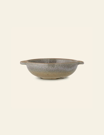 The Bloomingville Hariet Bowl by Bloomingville is a shallow, round stoneware bowl with small side handles and a speckled gray and beige glaze. Handcrafted details bring subtle charm to this piece, shown against an off-white background.