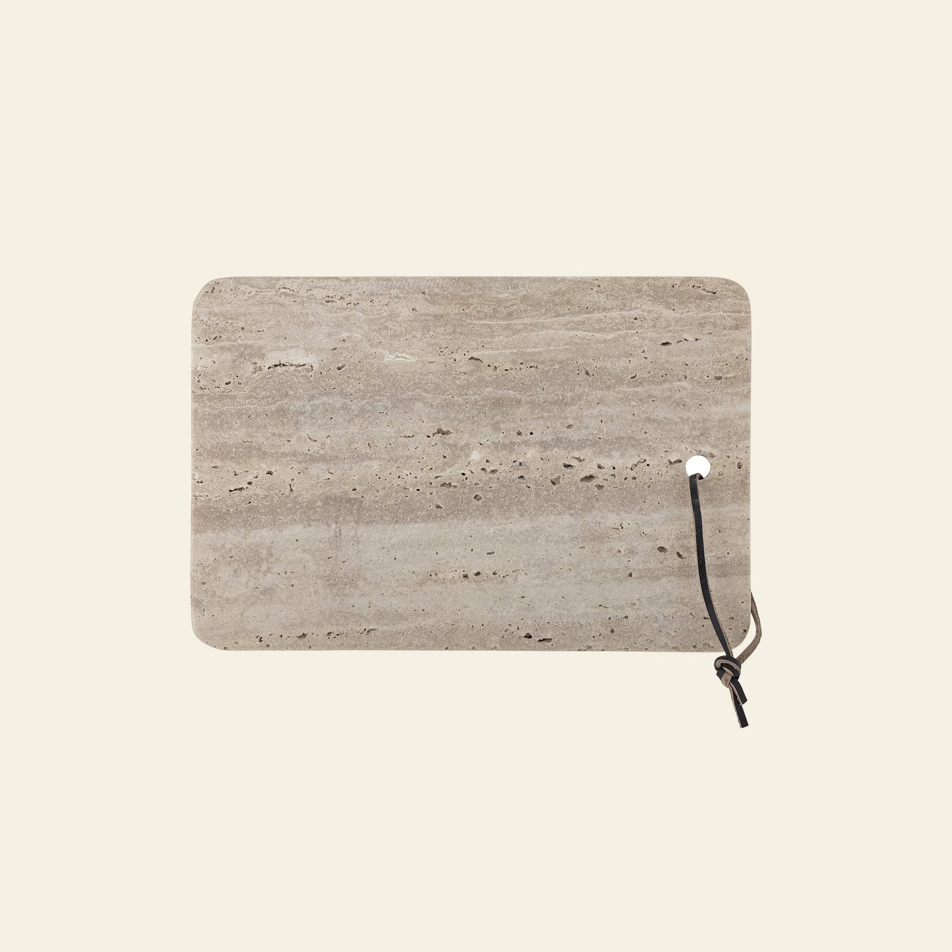 The Bloomingville Izabel Cutting Board by Bloomingville features a rectangular travertine design with unique natural veining, rounded corners, and a black leather loop—an ideal decorative kitchen accent against any light background.