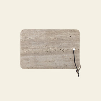 The Bloomingville Izabel Cutting Board by Bloomingville features a rectangular travertine design with unique natural veining, rounded corners, and a black leather loop—an ideal decorative kitchen accent against any light background.