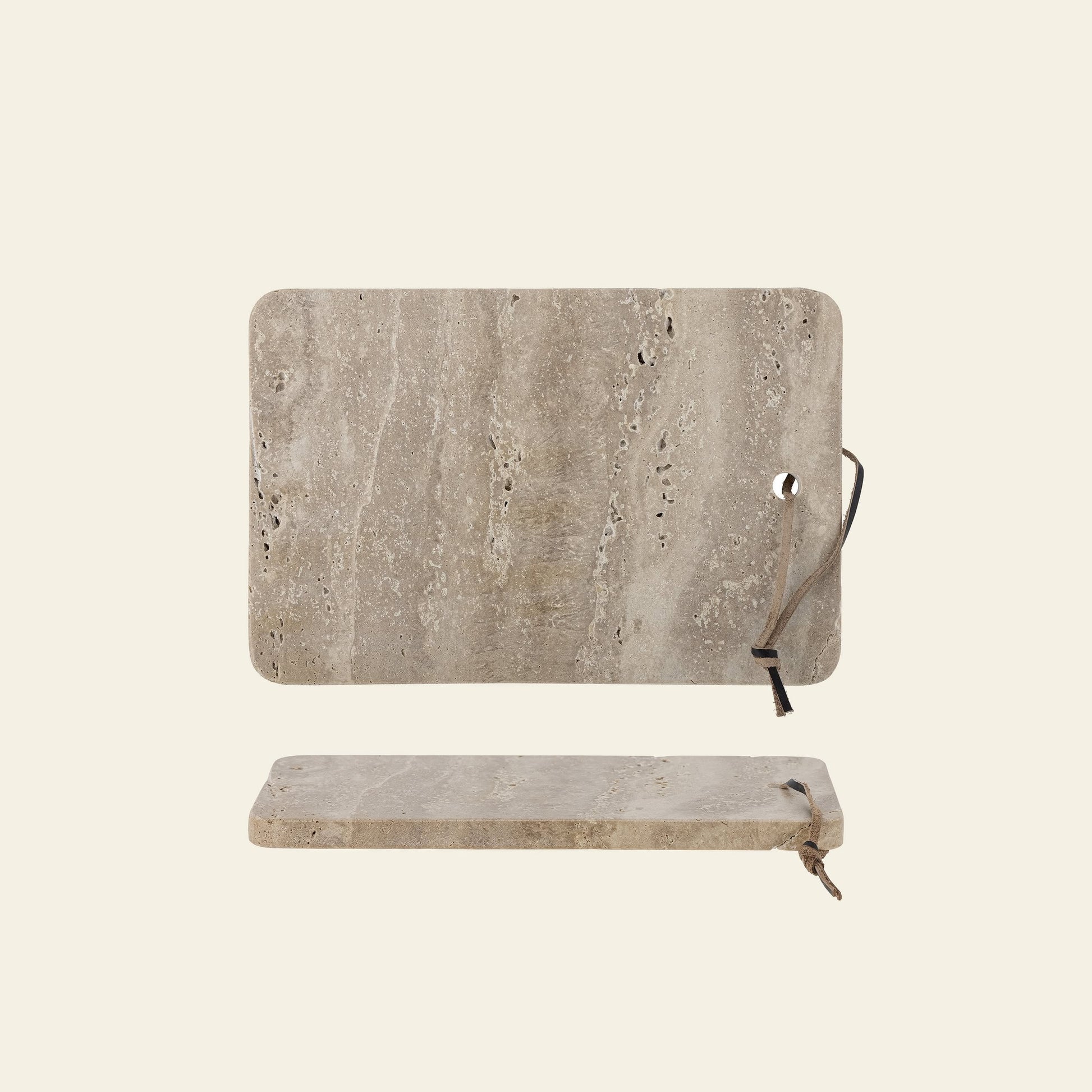 The Bloomingville Izabel Cutting Board by Bloomingville features two rectangular travertine boards with rounded corners and natural veining; one stands upright with a leather loop, while the other lies flat, creating a stylish kitchen accent.