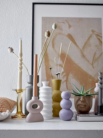 A sculptural display featuring the Bloomingville Kip Vase, twisted candlesticks, and a small aloe in a face-shaped pot sits on a shelf before framed abstract figure art, embodying Scandi style.