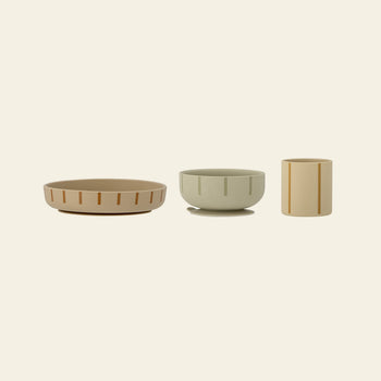 The Bloomingville Levi Tableware Set by Bloomingville features three minimalist ceramic pieces—a shallow tan bowl, sage green bowl, and beige cup—each with vertical lines, arranged stylishly on a light background.