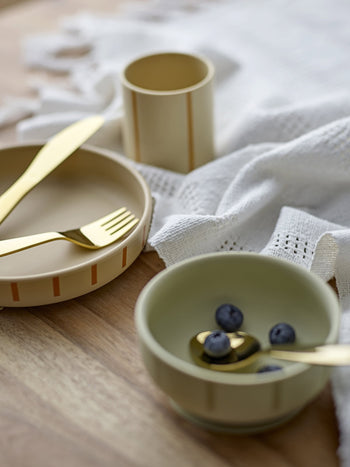 The Bloomingville Levi Tableware Set features two ceramic bowls—one with blueberries and a gold spoon, the other with a gold fork and knife—on a wooden table near a white textured cloth and beige cup. Perfect gift for young children.
