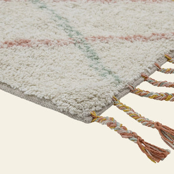Close-up of the Bloomingville Lilou Rug by Bloomingville, a textured cream childrens rug with pastel pink and green lines and multicolored twisted tassels along the edge, shown against a light backdrop.