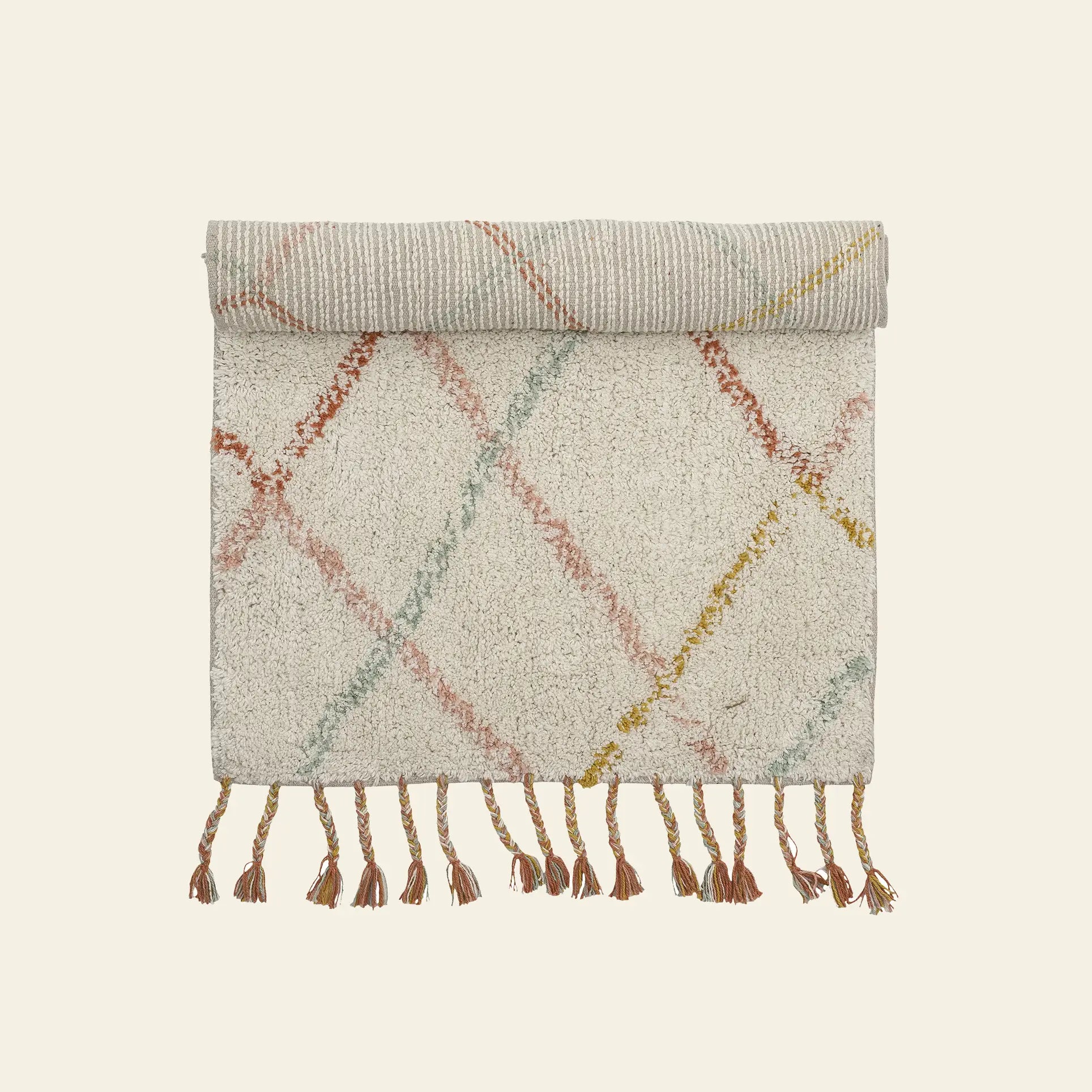 The cream Bloomingville Lilou Rug features pastel pink, yellow, and red diagonal lines, is rolled at the top with tassels along the bottom edge—ideal for adding color to a child’s room.