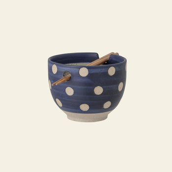 The Bloomingville Masami Bowl w/Chopsticks is a blue stoneware piece with white polka dots, a natural-colored base, and includes a notch and hole for resting the wooden chopsticks across the top.