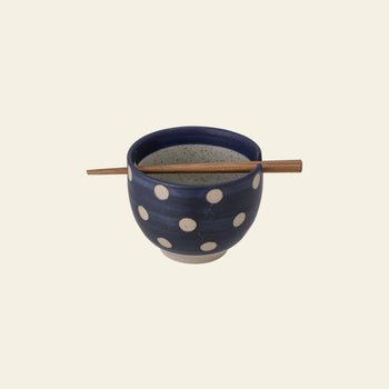 The Bloomingville Masami Bowl w/Chopsticks features blue stoneware with white polka dots and wooden chopsticks resting across the top, making it a charming kitchenware addition from Bloomingville.