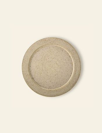 The Bloomingville Nugga Plate by Bloomingville is a round, beige stoneware plate with a speckled pattern and ridged rim—an ideal choice for serving outdoor meals on a light, neutral backdrop.
