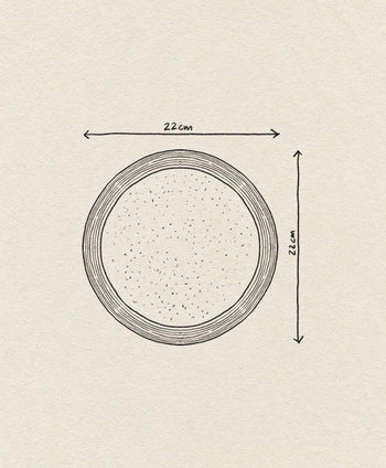 A hand-drawn illustration of the Bloomingville Nugga Plate, a 22 cm stoneware plate by Bloomingville, shown from above with labeled measurements on light textured paper, evoking an inviting outdoor meal setting.