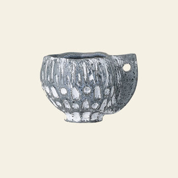 The Bloomingville Oney Flowerpot by Bloomingville is a small, handmade ceramic piece with a rough gray and white finish, rounded body, and flat handle with a circular hole—ideal as a decorative flowerpot cover against any plain beige background.