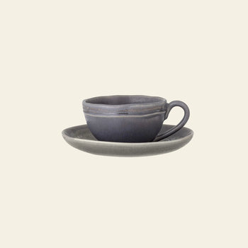The Bloomingville Raben Cappuccino Cup With Saucer by Bloomingville, in elegant dark gray stoneware with a handle, is displayed on a matching saucer against a plain cream background.