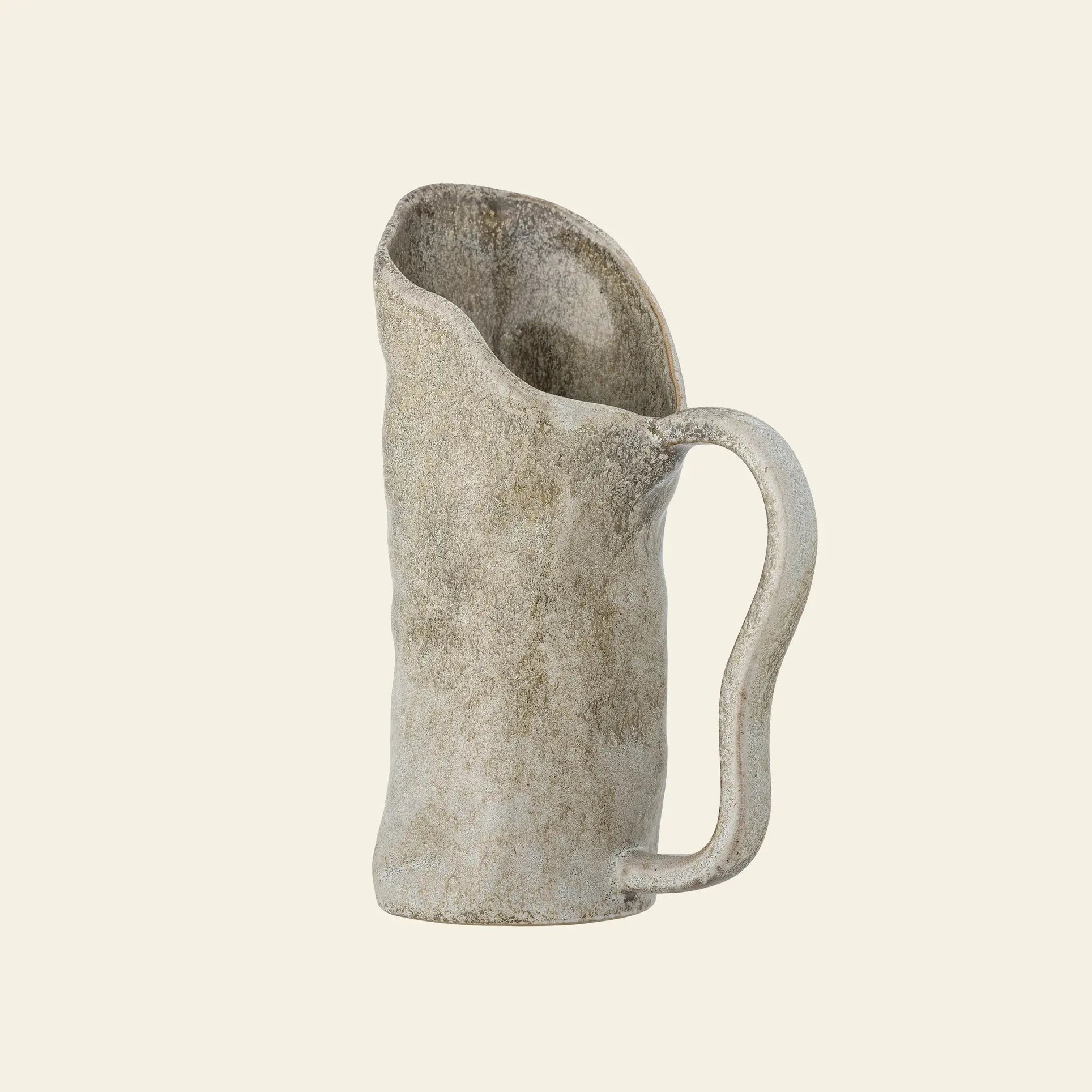 The Bloomingville Razan Jug by Bloomingville is a rustic, textured handmade piece with an asymmetrical rim and large handle in a natural earthy hue, photographed against a plain light background.