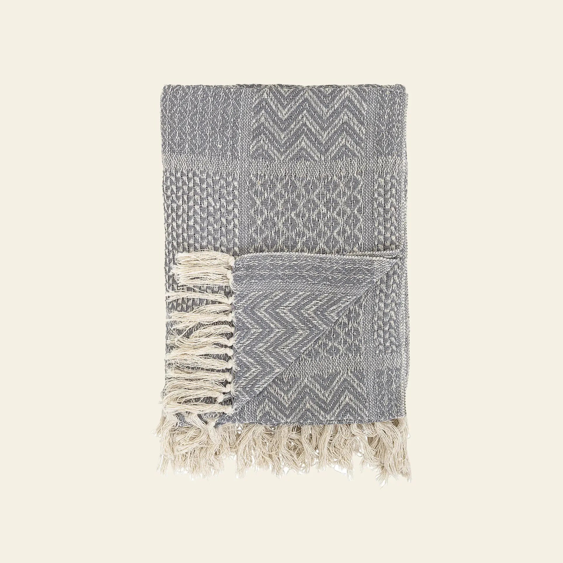 The Bloomingville Rodion Throw by Bloomingville features gray and cream chevron and geometric patterns with fringe on both ends, adding comfort and style to your decor. Shown folded on a plain light background.