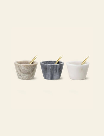 Three Bloomingville Rosamynthe Salt Jars with gold spoons—beige, dark gray, and white—are arranged side by side on a plain background, ideal for serving spices.