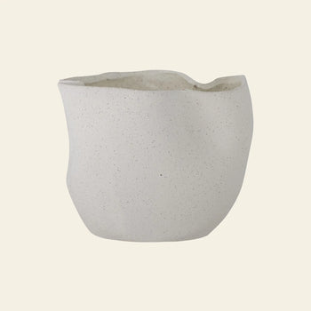 The Bloomingville Sanam Flowerpot by Bloomingville features an off-white stoneware finish with a rough, uneven surface and an irregular, organic shape, creating a contemporary look against a plain light background.