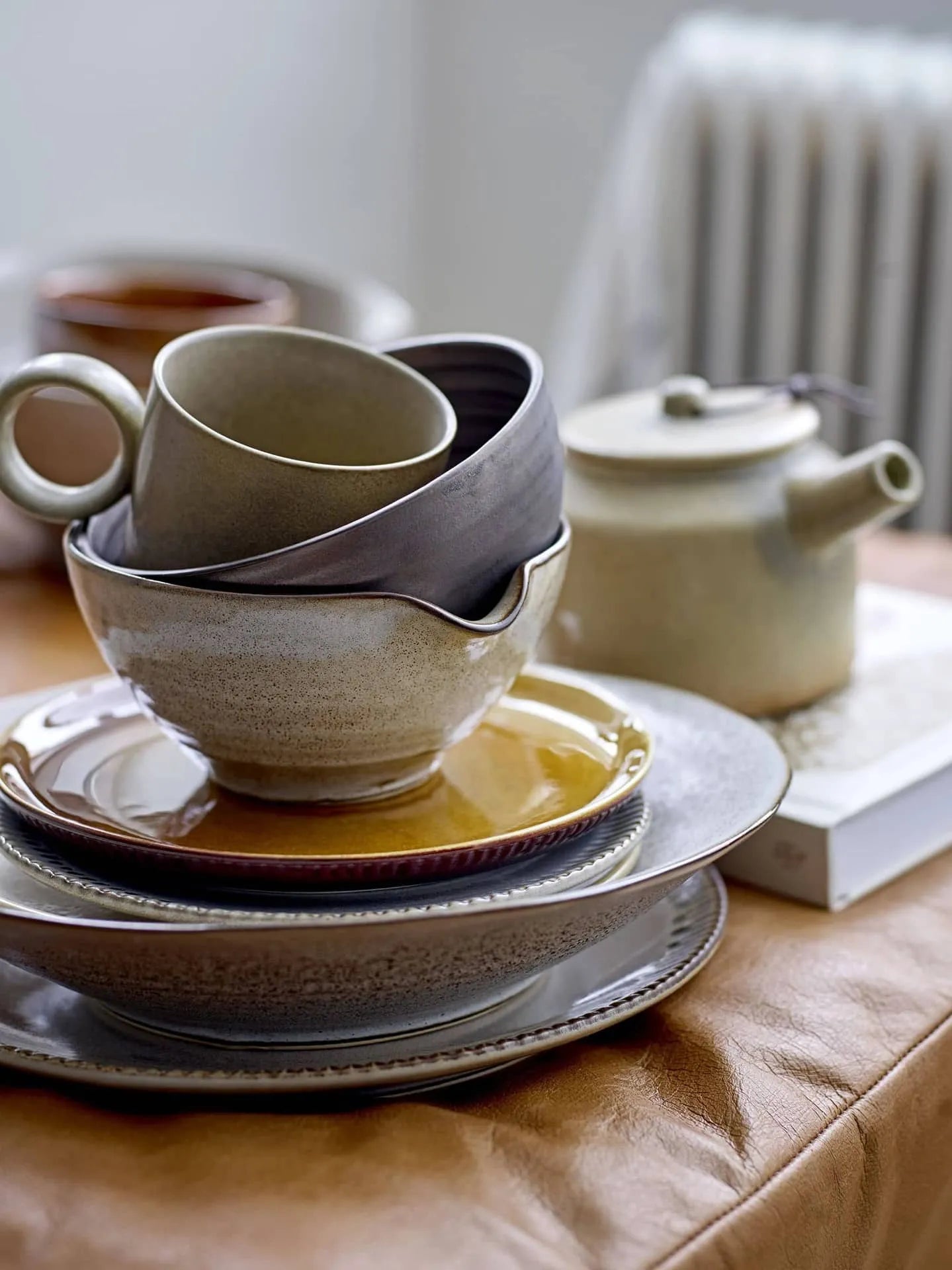The Bloomingville Thea Plate by Bloomingville, styled in earthy tones with a rustic brown design, rests on a leather surface alongside matching tableware and a teapot, creating a warm, inviting scene.