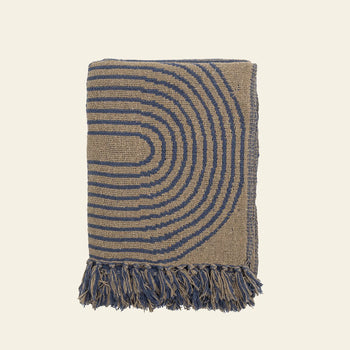 The Bloomingville Tiffanie Throw by Bloomingville is a folded blue and beige cotton blanket with a repeating semicircular arch pattern and blue fringed tassels along the bottom edge, shown on a plain background.