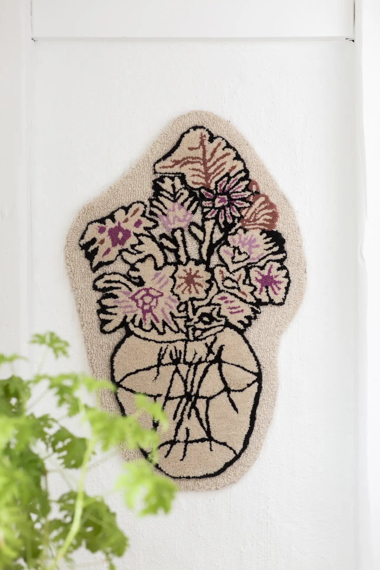 The Bongusta Autumn Flowers Rug by Bongusta is a 100% wool wall hanging, featuring a textured vase with abstract, colorful flowers outlined in black on an off-white background and leafy green plant details in the lower left corner.