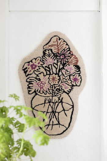 The Bongusta Autumn Flowers Rug by Bongusta is a 100% wool wall hanging, featuring a textured vase with abstract, colorful flowers outlined in black on an off-white background and leafy green plant details in the lower left corner.