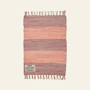 The Bongusta Chindi Rug (45x60) is handcrafted in India from surplus cotton with pink horizontal bands, off-white background, and fringe on the short ends. A small fabric label accents one corner. Brand: Bongusta.
