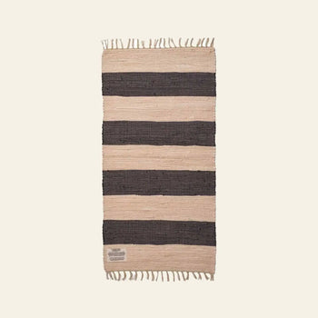 The Bongusta Chindi Rug (60x120) by Bongusta is a rectangular rug handcrafted in India from surplus cotton, with wide black and beige stripes and short fringe on the ends, shown against a plain light background.