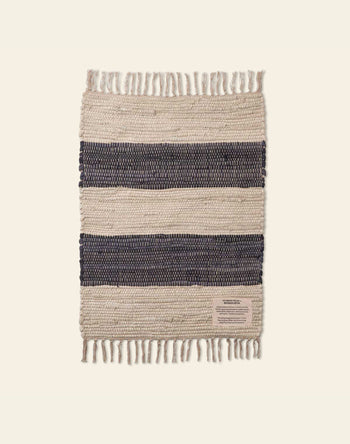 The Bongusta Chindi Rug (45x60) by Bongusta is a rectangular, handcrafted Indian rug with fringed edges, alternating cream and dark navy blue stripes, made from surplus cotton and finished with a small beige label on one corner.