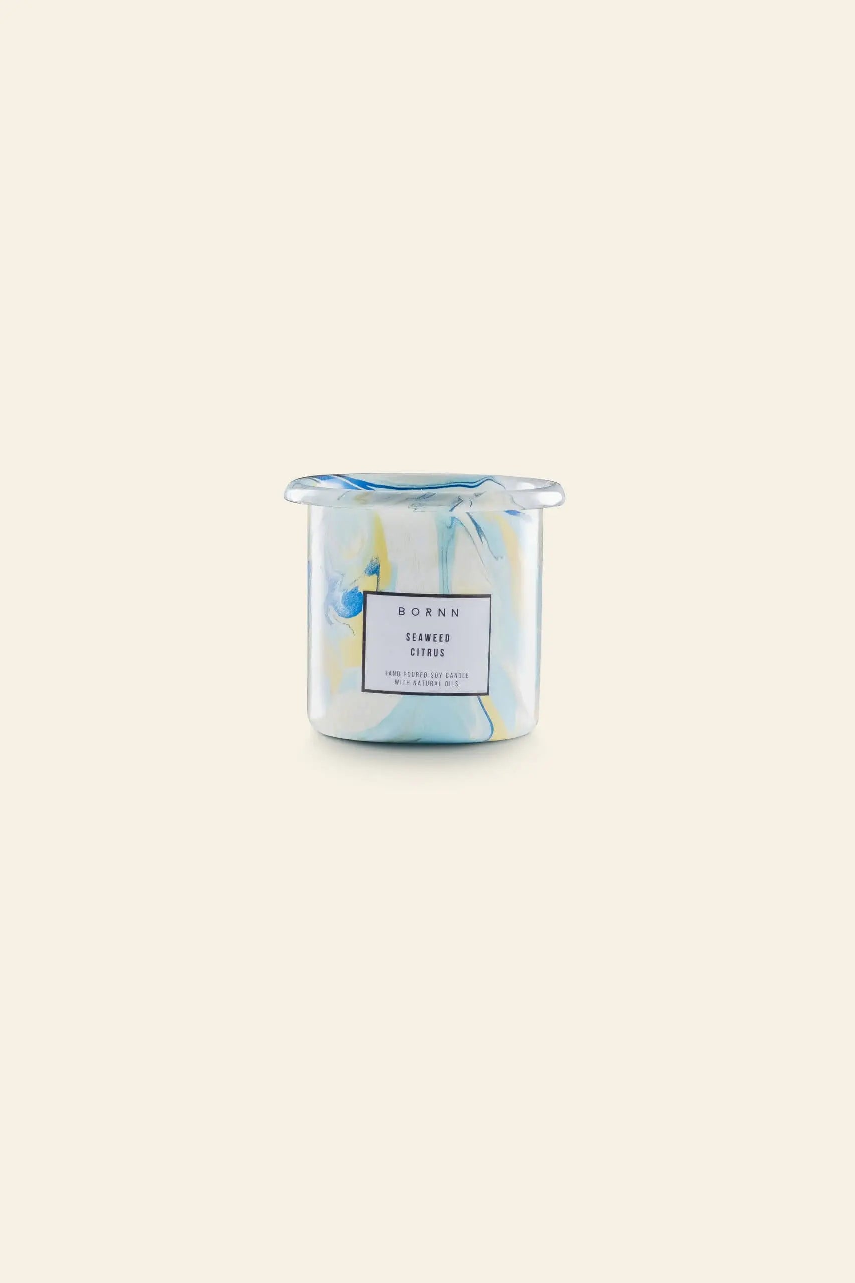 A marbled blue, yellow, and white cylindrical container holds a Bornn Enamelware Candle in Seaweed-Citrus scent by Bornn Enamelware. The candle sits against a plain light beige background.