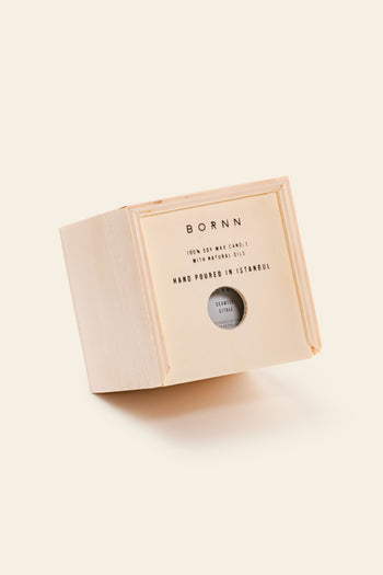 A beige, cube box labeled Bornn Enamelware Candle Seaweed-Citrus rests on its edge against a cream background. A small round window shows the candle inside. The box states 100% soy wax with mineral oils, hand poured in Istanbul.