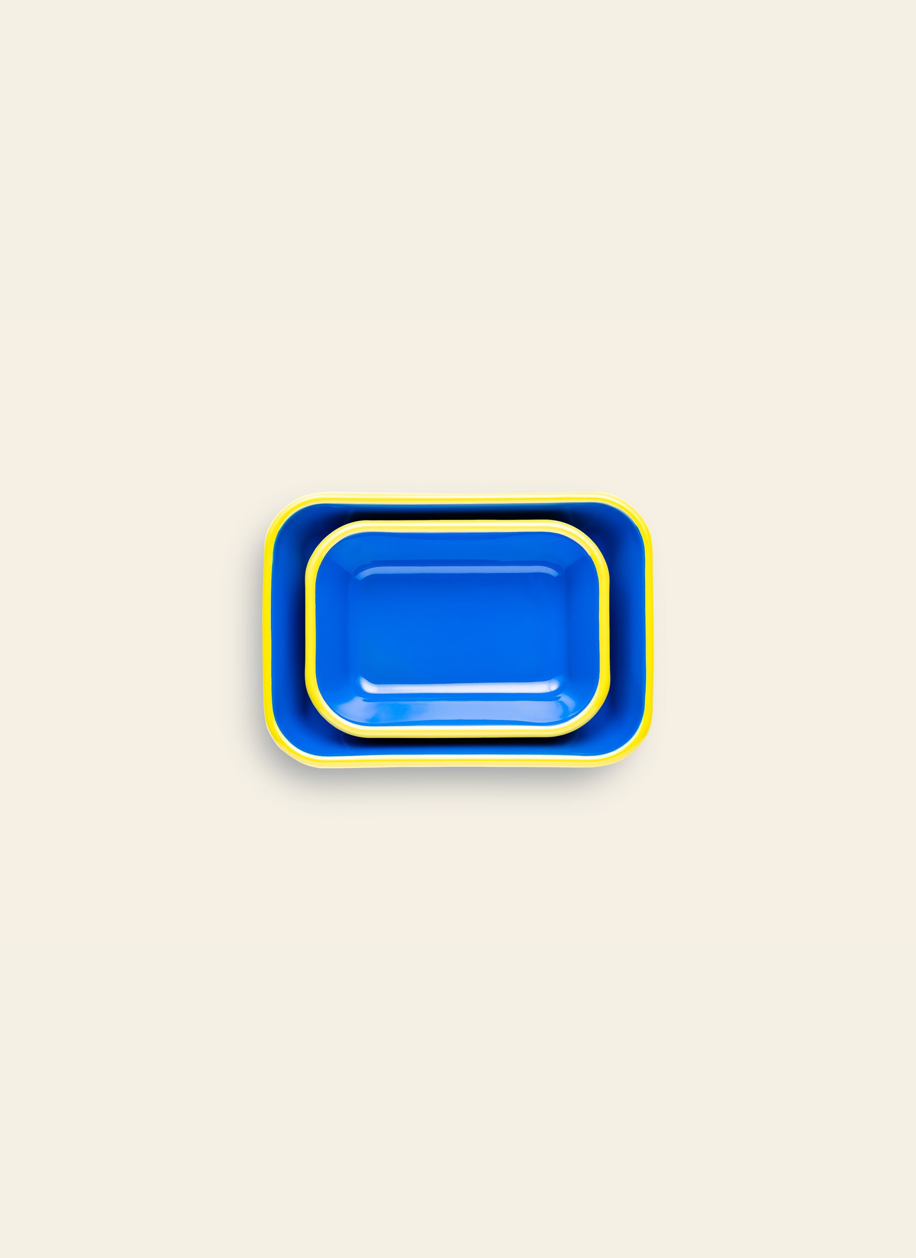 A medium blue Bornn Enamelware Colorama Baking Dish with a yellow rim is nested inside a larger tray, both placed on a plain light beige background.