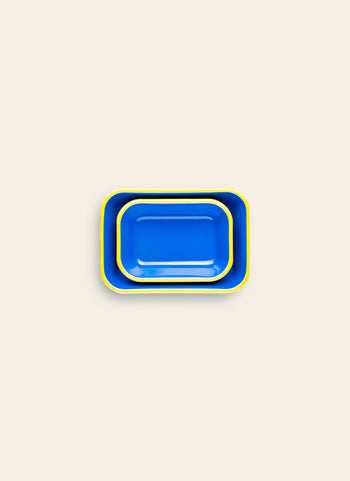 A medium blue Bornn Enamelware Colorama Baking Dish with a yellow rim is nested inside a larger tray, both placed on a plain light beige background.