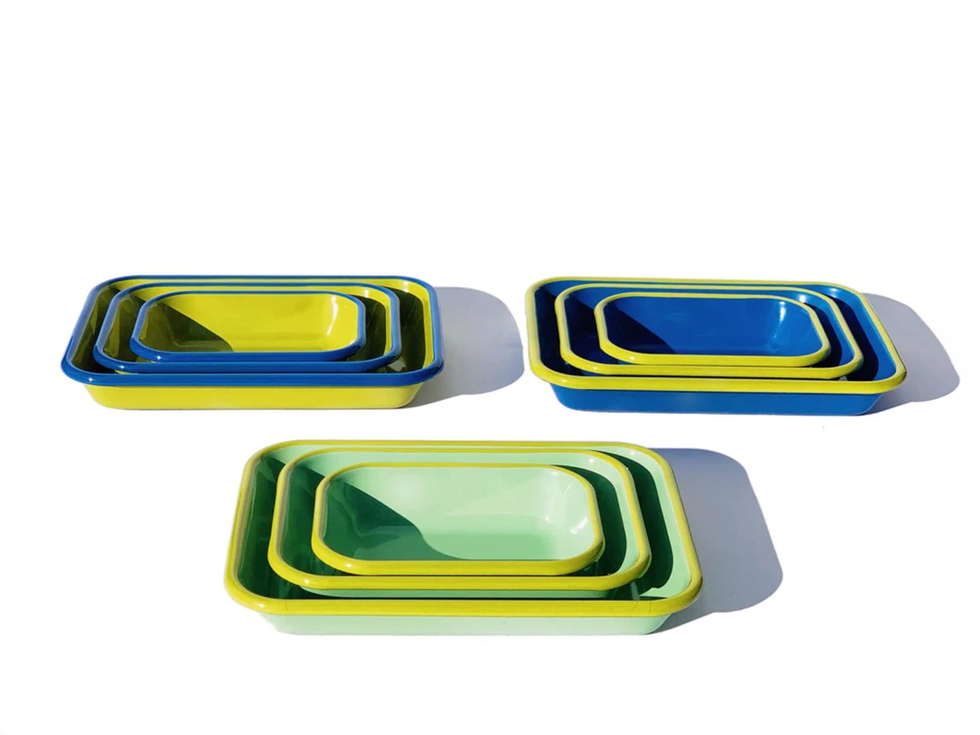 The Bornn Enamelware Colorama Baking Dish, Medium, is shown in vibrant blue, yellow, and green, with trays of different sizes stacked inside each other on a white background and shadows cast to the right.